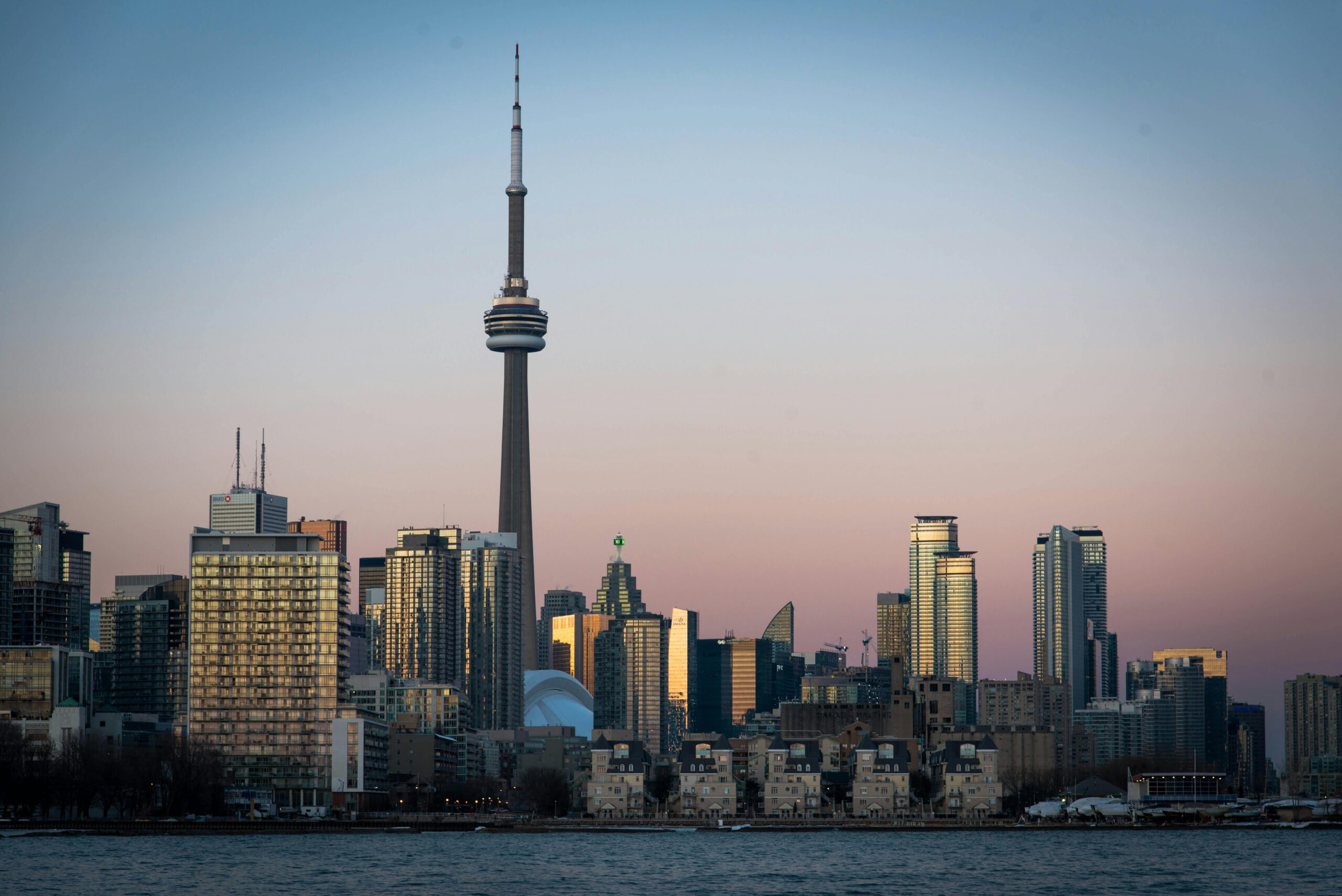 View of Toronto skyline featuring the CN Tower during dusk with cityscape reflections on Lake Ontario.